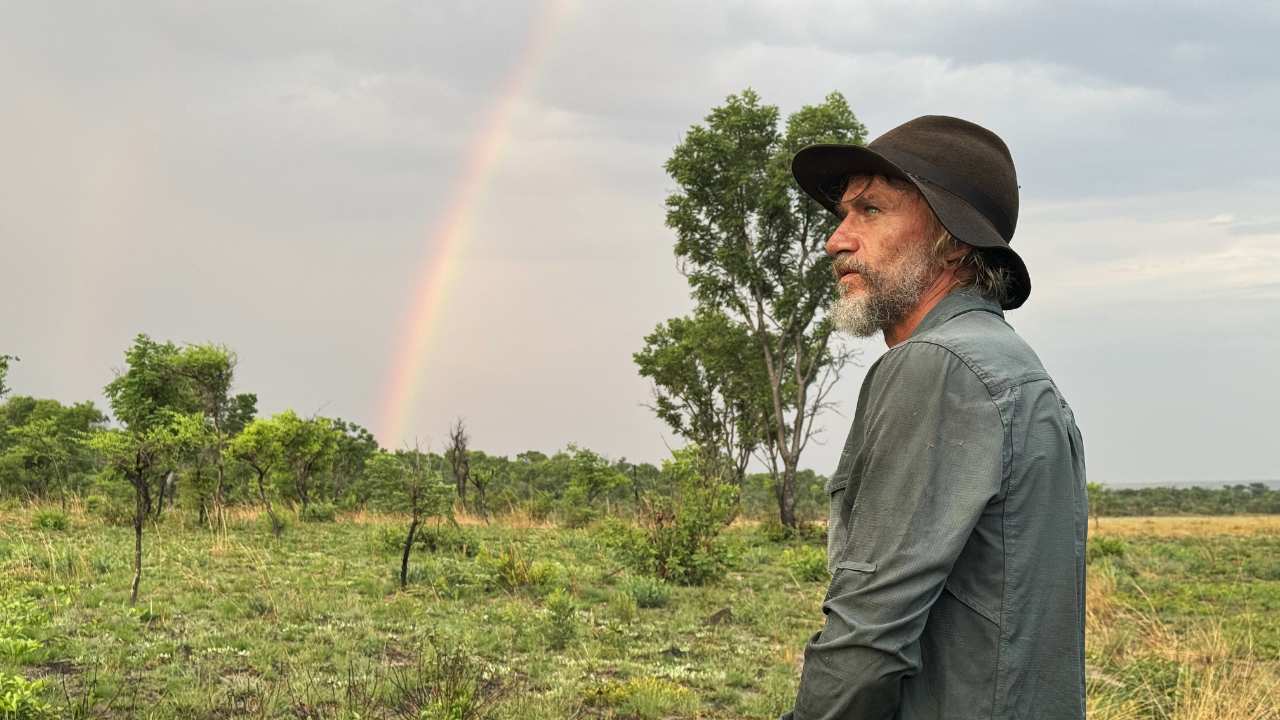 a man with a beard and hat in front of a rainbow